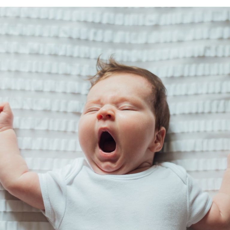 Baby liegt im Bett und gähnt.